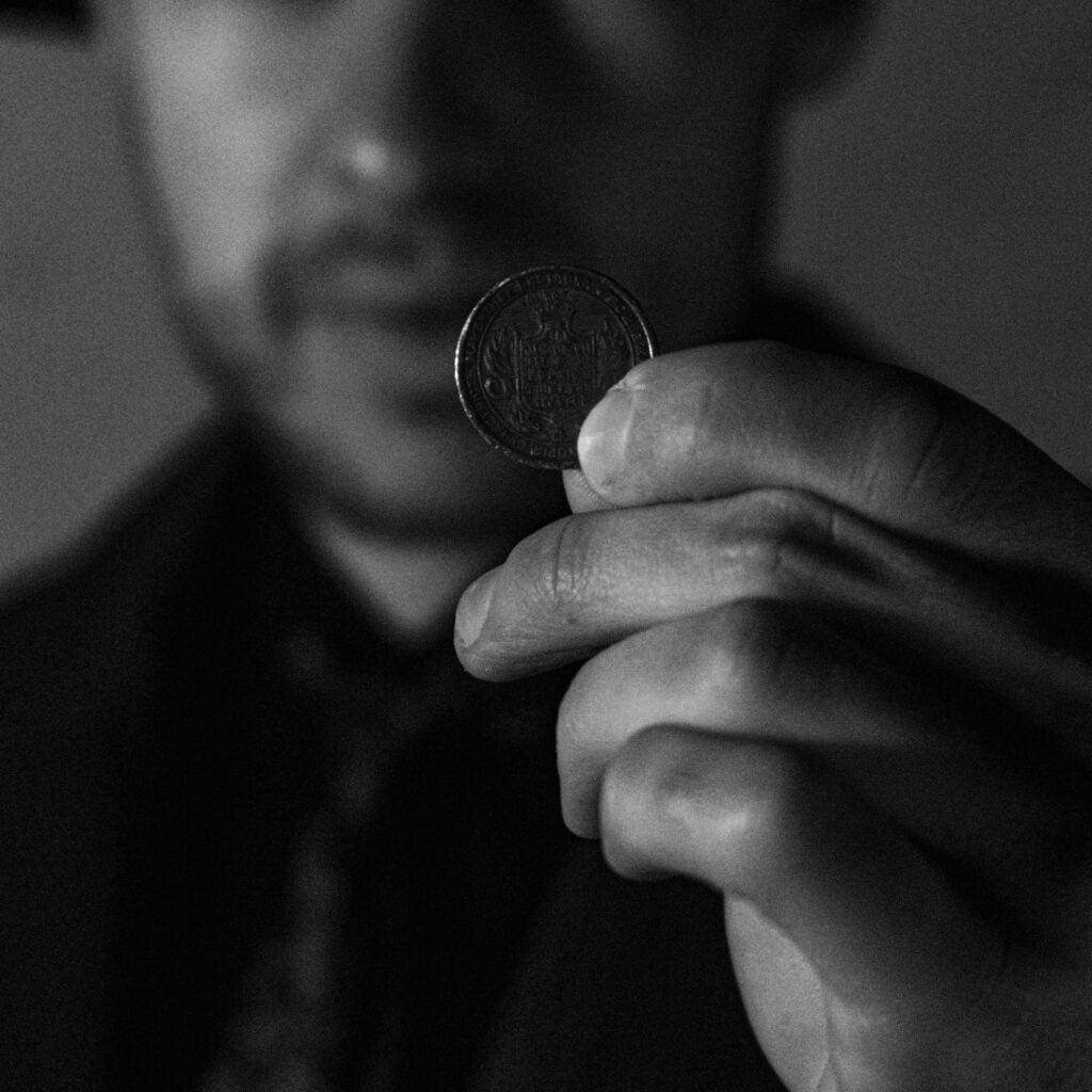 10 Way to Save Money A man holds a coin close to the camera in a dramatic black and white image.